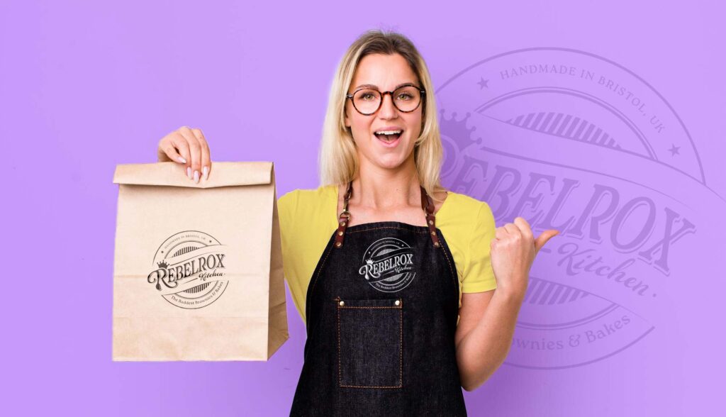 smiling blonde baker holding a brown paper bag.jpg